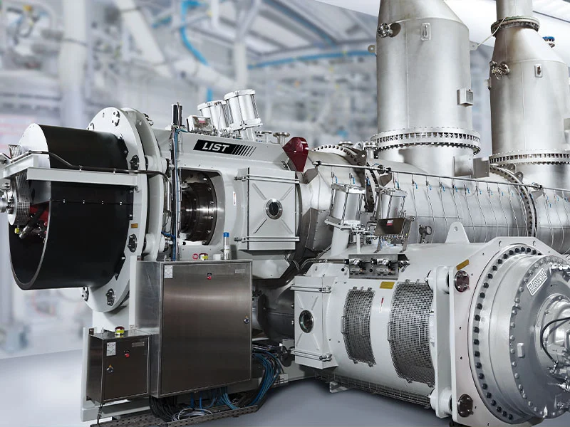 single-shaft-kneader-reactor-with-plant-in-background LIST Single Shaft KneaderReactor in white with plastic processing plant in the background